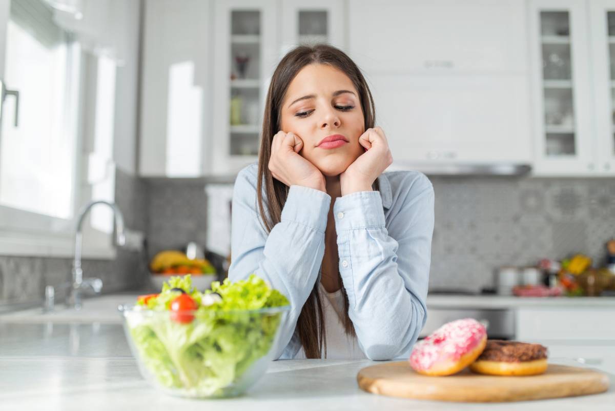 Woman deciding between eating apples or sugary donuts that cause plaque buildup.